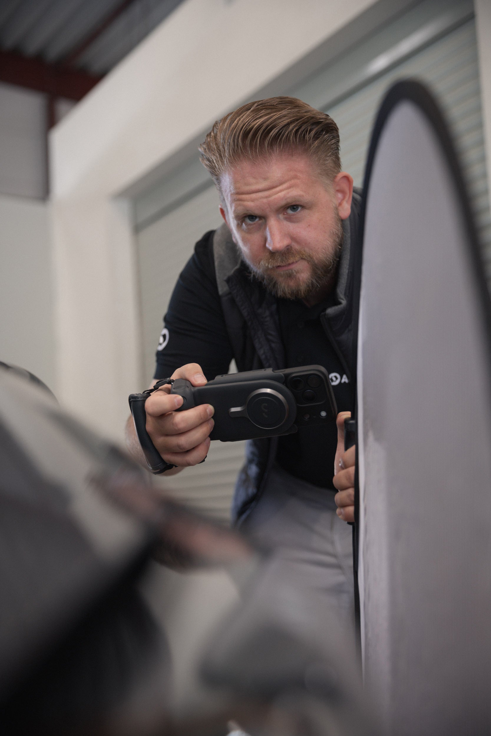 Lars Jacobi, Kfz-Sachverständiger von AUTONORM, fotografiert mit Kamera und Dellenspiegel eine Fahrzeugbeschädigung.