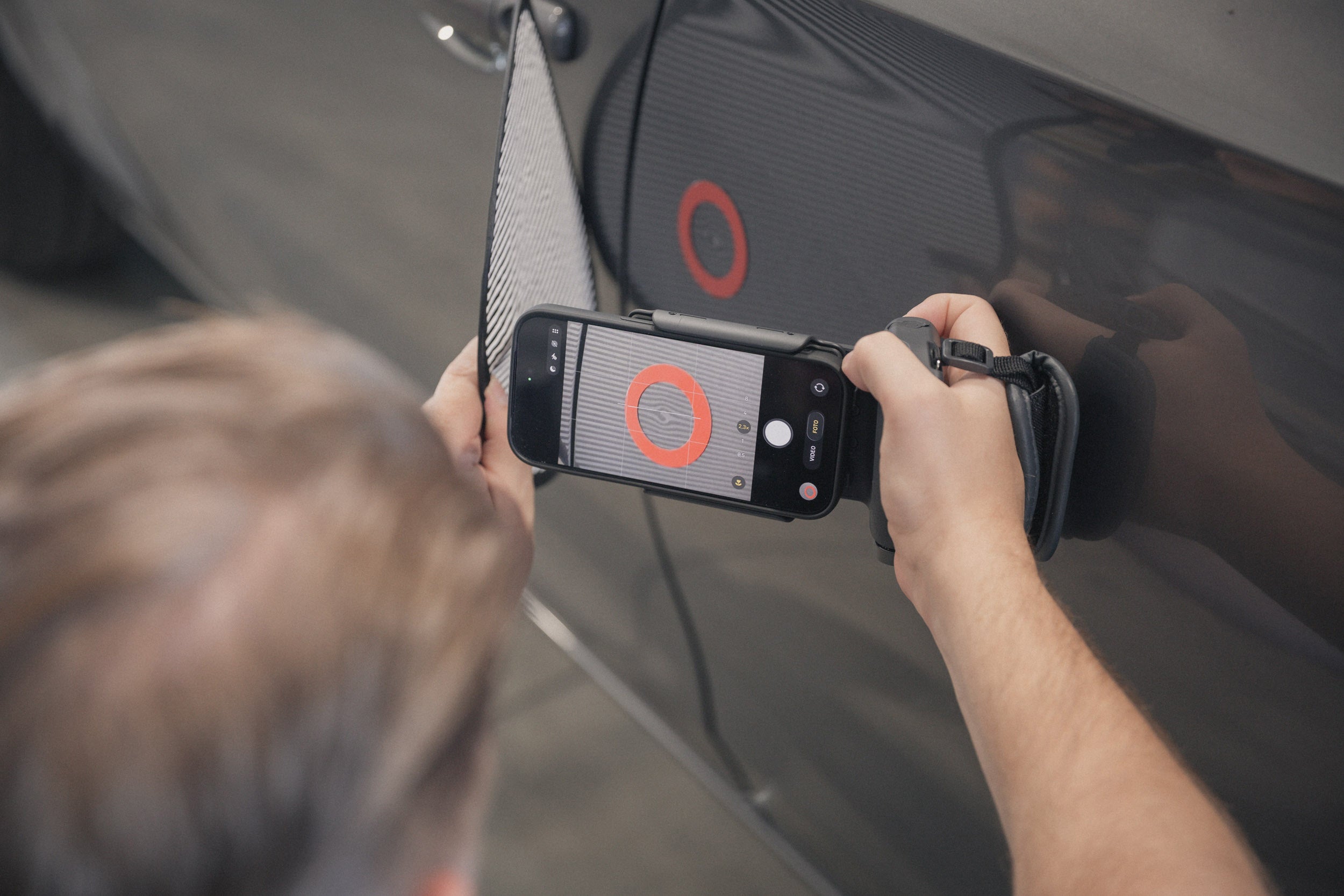 Prüfung der Lackoberfläche mit Dellenspiegel und Smartphone auf kleinste Beschädigungen beim Gebrauchtwagencheck.