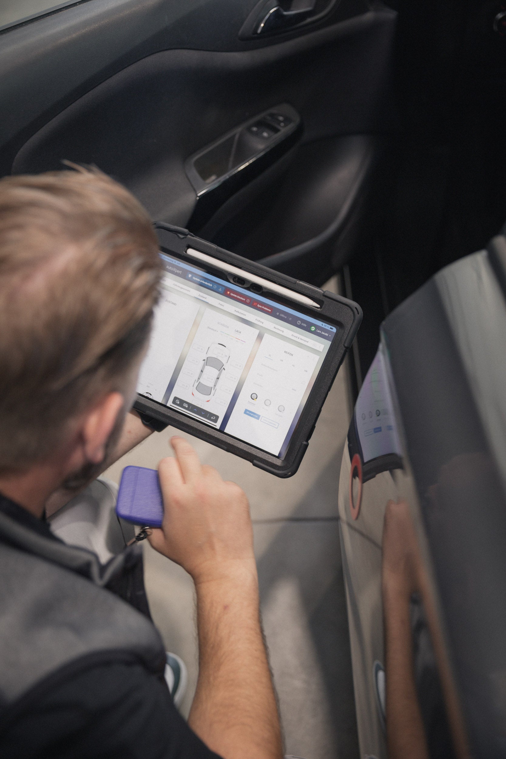 Lars Jacobi misst bei einer Fahrzeugbewertung die Lackschichtdicke am Einstiegsbereich und dokumentiert die Werte im Tablet.