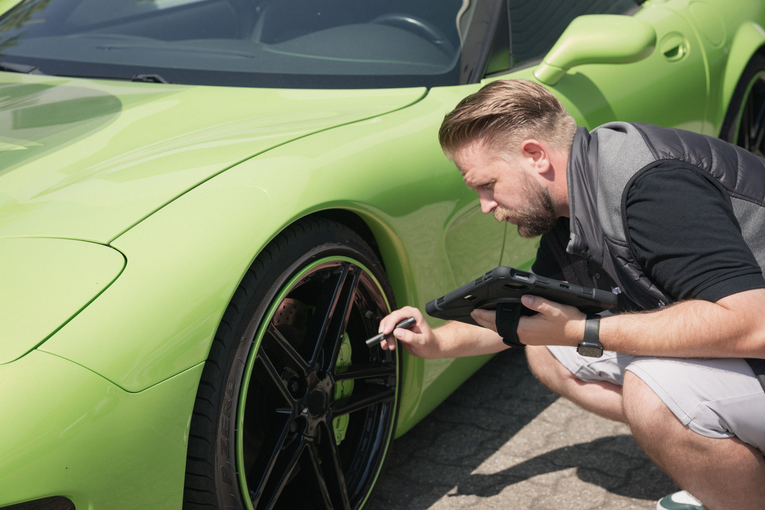 Lars Jacobi prüft bei einem Gebrauchtwagencheck mit dem Tablet Felgen und Bremsanlage einer giftgrünen Corvette.