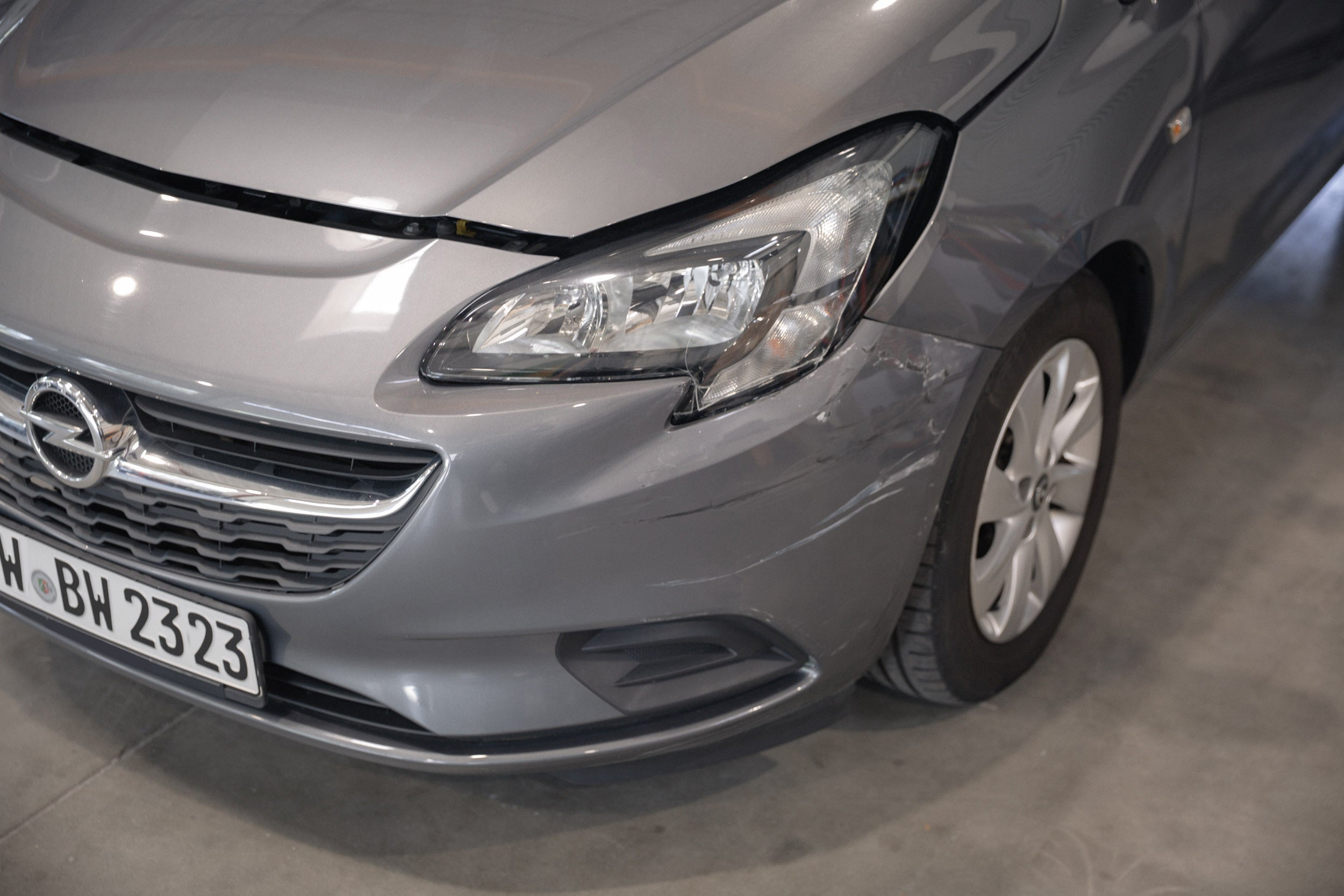 Nahaufnahme eines Unfallschadens am vorderen Kotflügel eines silbernen Opel Corsa.