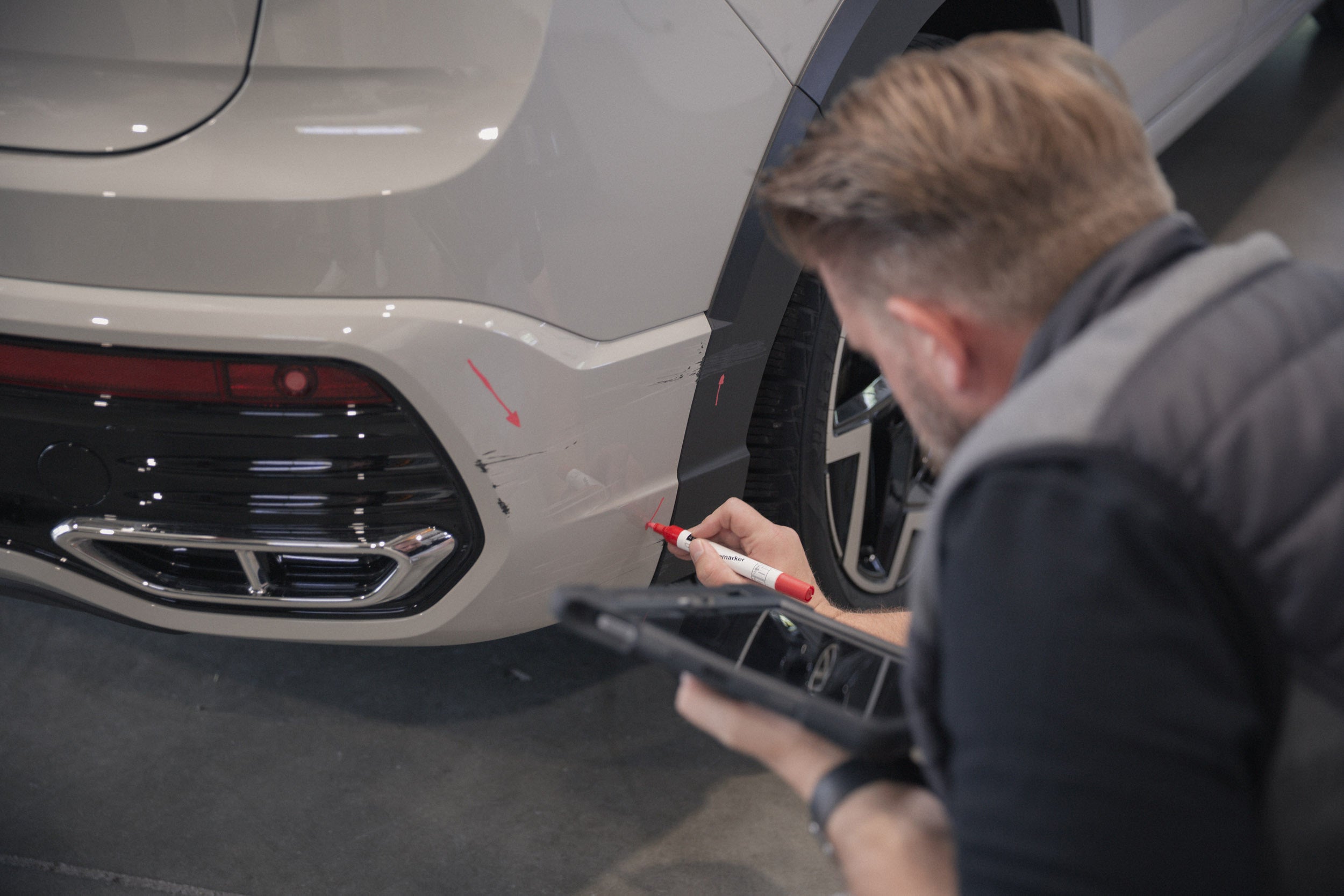 Lars Jacobi markiert beim Gebrauchtwagencheck einen Heckschaden an einem VW Taigo mit Kreidemarker und dokumentiert ihn mit dem Tablet.